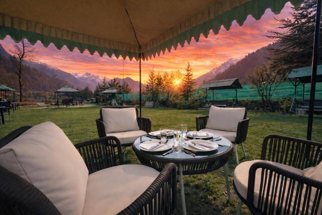a table and chairs under a tent with a sunset at Hotel The Himalayan Riverside - Most Awarded Property of Manali 2025-26 in Manāli