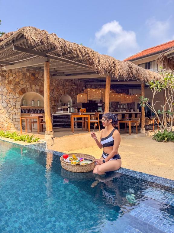 a woman in a bikini sitting next to a swimming pool at Serendipity Mirissa in Mirissa