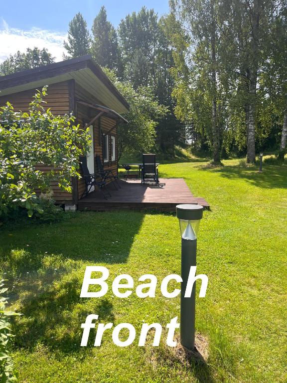 a log cabin with a beach front sign in the grass at Katase Tiny House, Secluded Beachfront Cabin on Lake Peipus in Katase