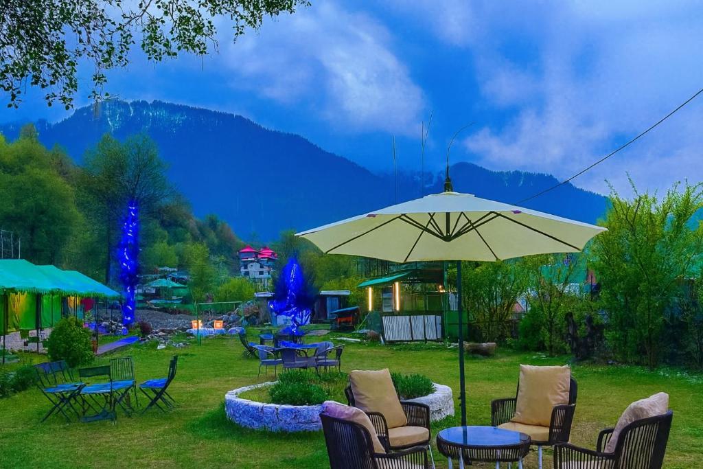 a patio with a table and chairs and an umbrella at The Himalayan Swiss Cottage with Bonfire, Manali - A Riverside Retreat in Manāli