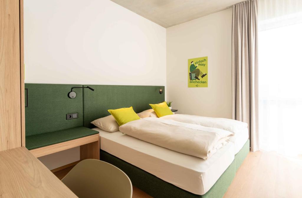 ein Schlafzimmer mit einem Bett mit grünem Kopfteil und gelben Kissen in der Unterkunft eee Hotel Laakirchen in Laakirchen