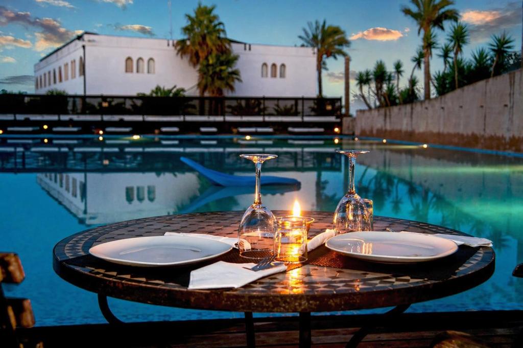a table with a candle and glasses on a table near a pool at Hotiday Otranto Baia Resort in Otranto