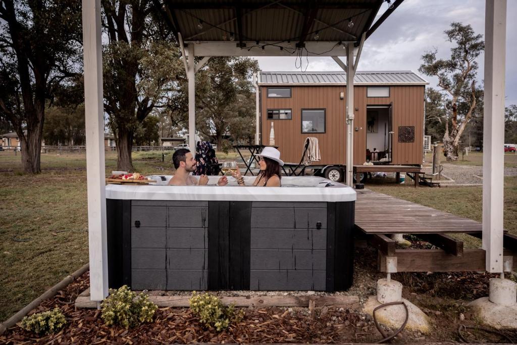 a man and woman in a bath tub in a backyard at Odyssean Tiny House B by Tiny Away in Cessnock