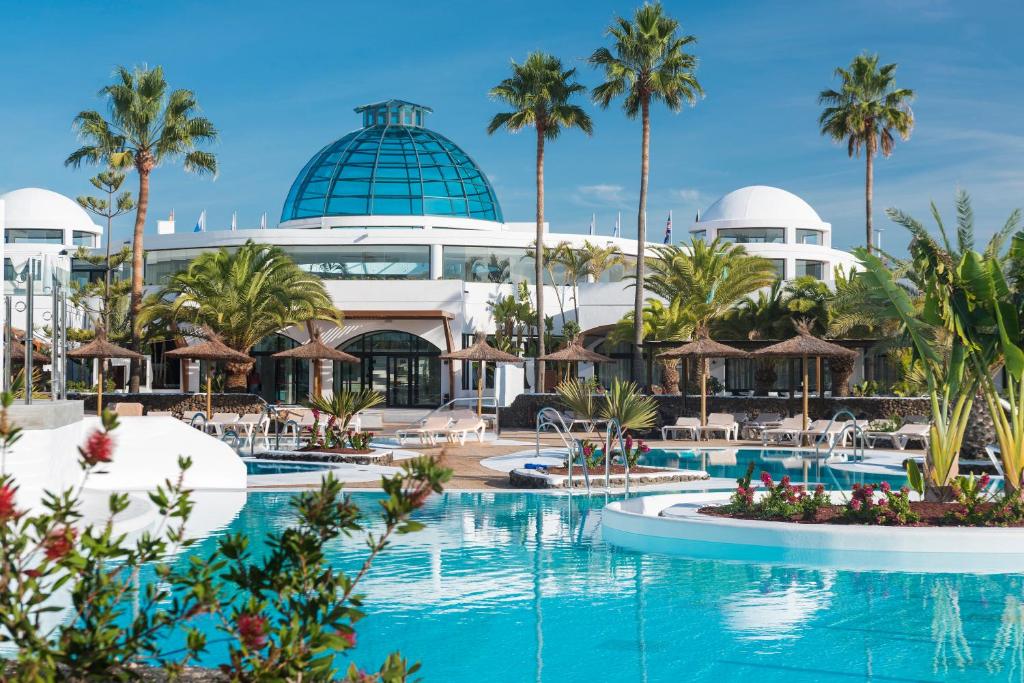 een resort met een zwembad en palmbomen bij Elba Lanzarote Royal Village Resort in Playa Blanca