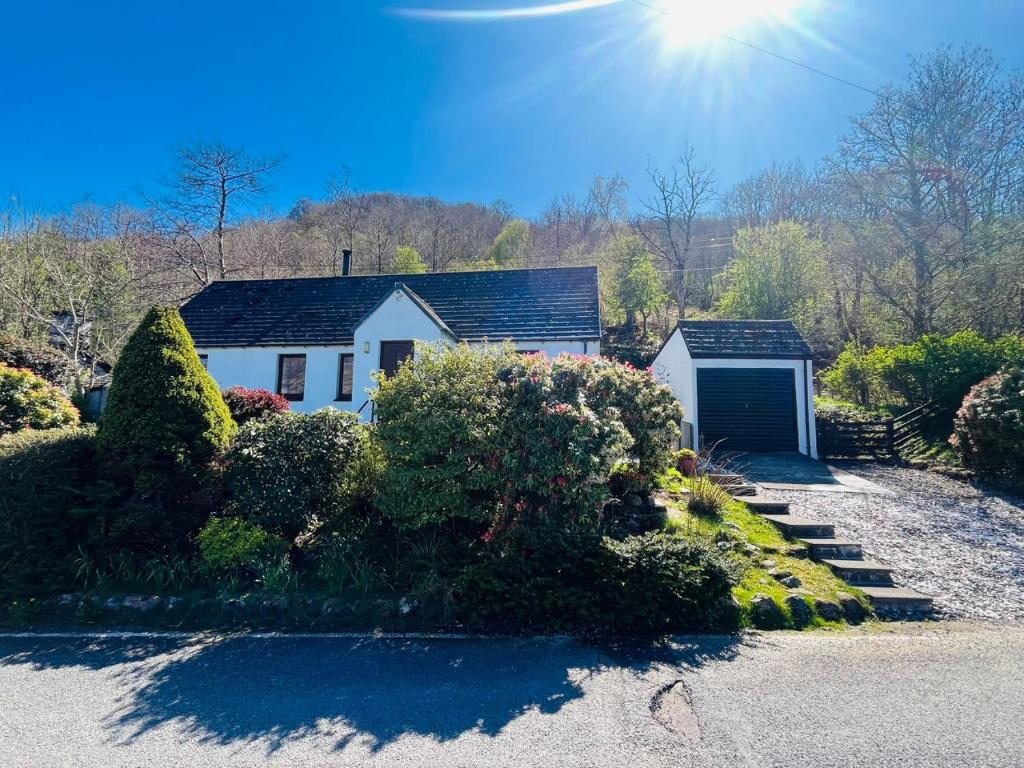 a white house with a garage and some bushes at Braehead Cottage in Glencoe