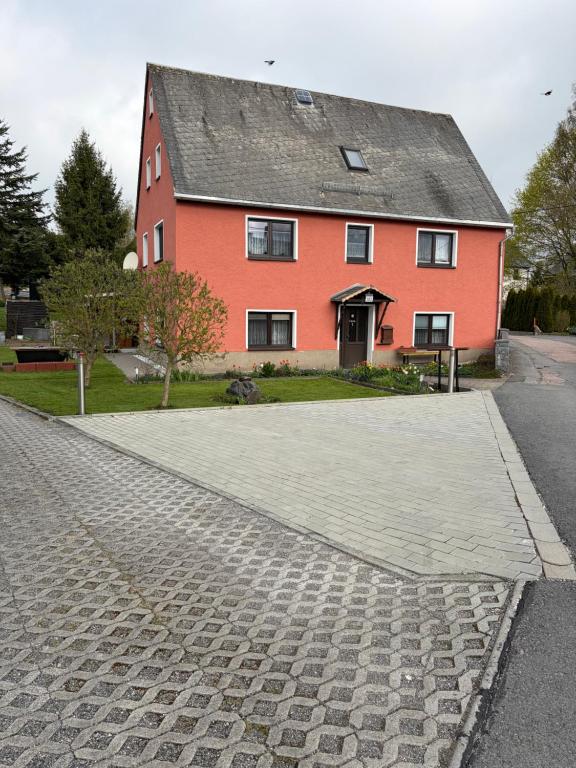 a red house with a cobblestone street in front at Ferienwohnung Lippmann in Großhartmannsdorf