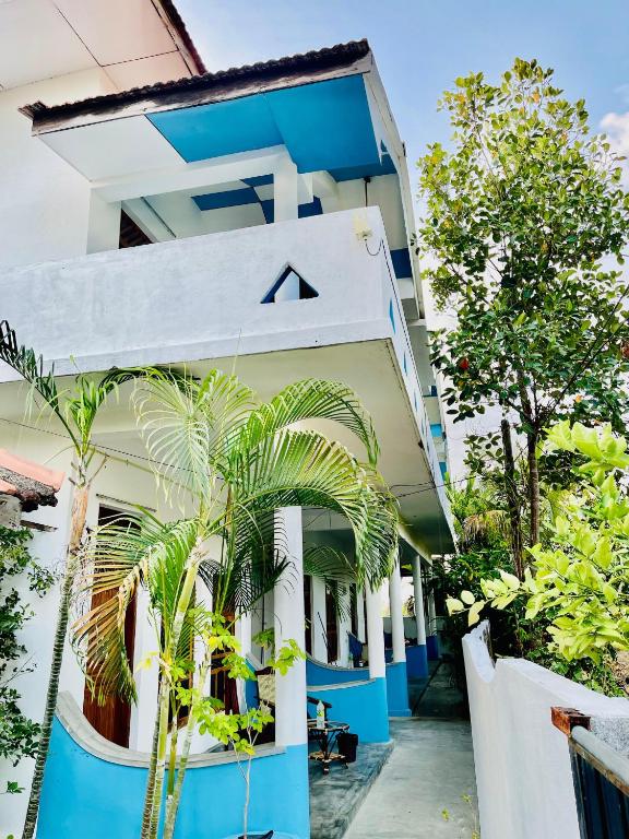 a blue and white building with a palm tree in front at Paradise Bay Hotel in Arugam Bay