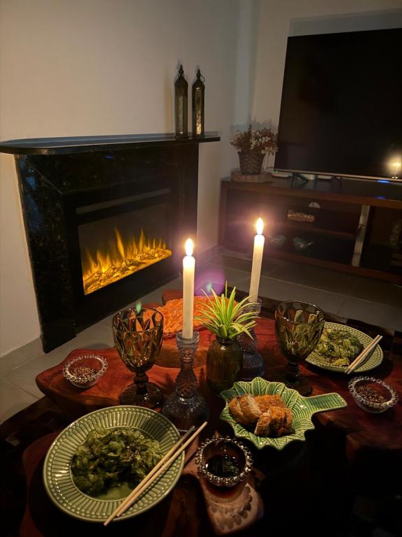 a table with candles and plates of food and a fireplace at Chalé Gravatá in Gravatá