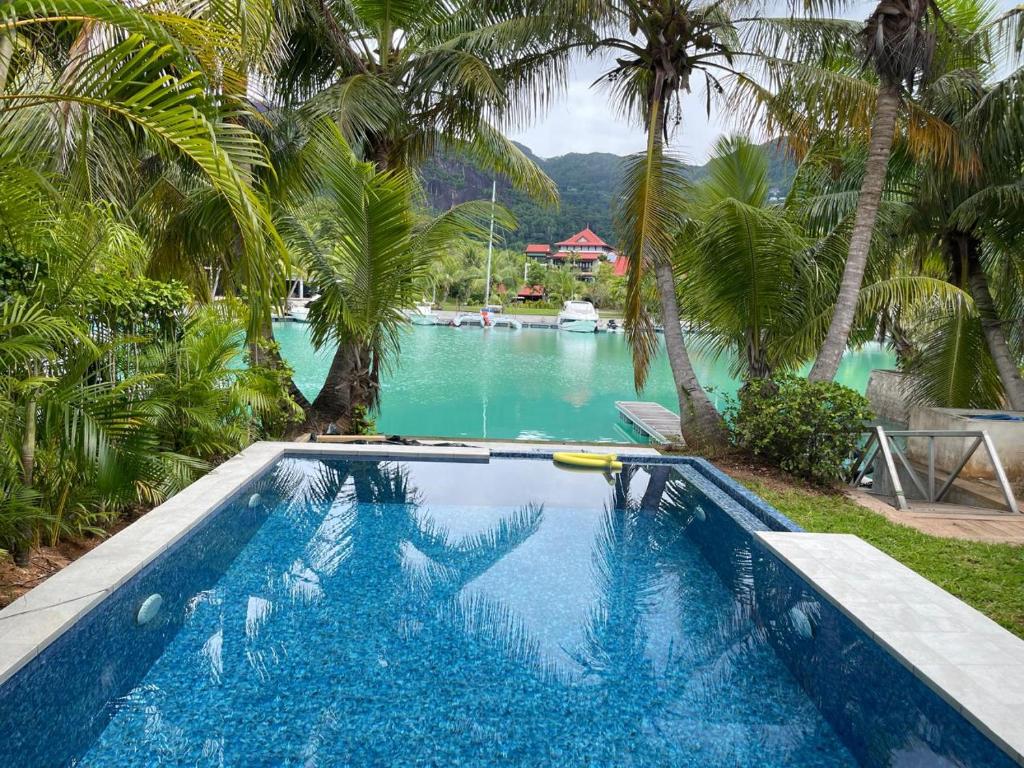 a swimming pool with palm trees and a body of water at Maison Cinnamon by Simply-Seychelles in Eden Island
