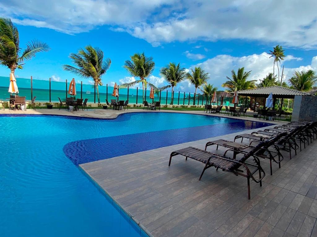 a pool with benches and the ocean in the background at Flat Premium Sea View - Tabatinga Beach in Conde
