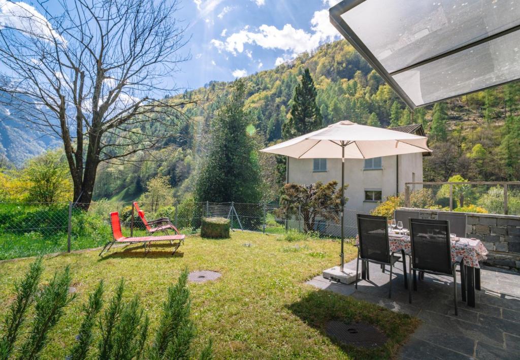 a patio with a table and chairs and an umbrella at Vallemaggia Green House in Sornico