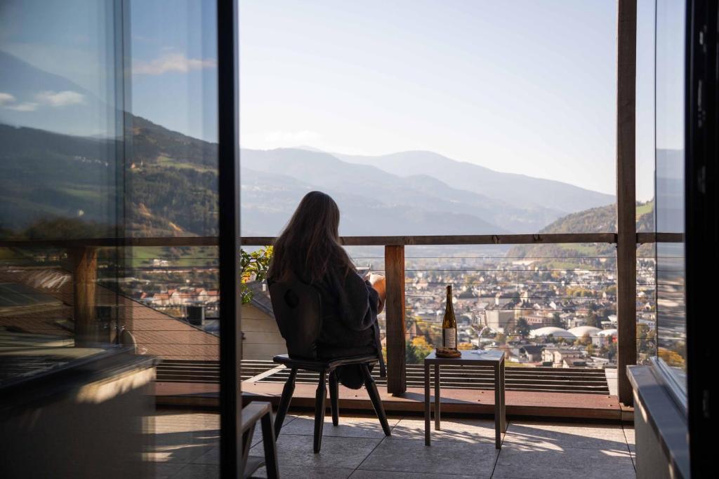 a woman sitting on a chair on a balcony looking at a city at byHaller Suites & AO Restaurant in Bressanone