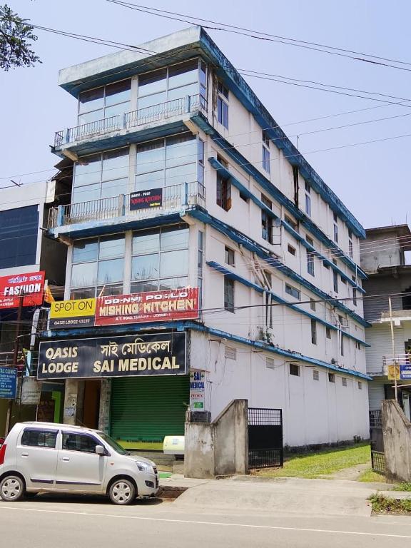 a white building with a car parked in front of it at Oasis Lodge in Jorhat