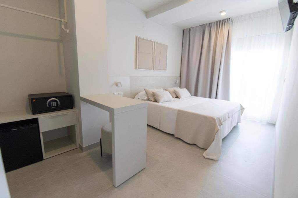 a white bedroom with a bed and a desk at Hotel Roca Plana in L'Ampolla