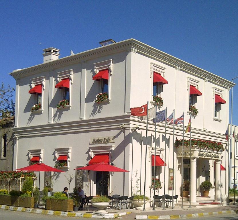 un edificio blanco con sombrillas rojas delante en Hotel Gelibolu, en Galípoli