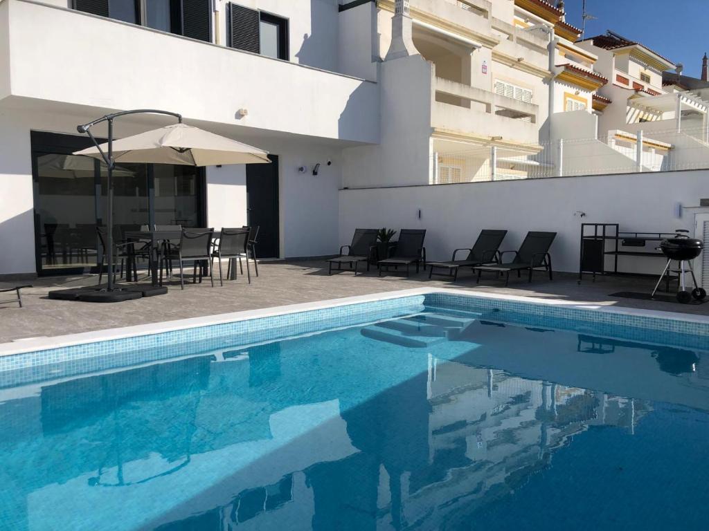a swimming pool with chairs and an umbrella next to a building at Casa Dulcelina Monte Gordo, Algarve, Portugal in Monte Gordo