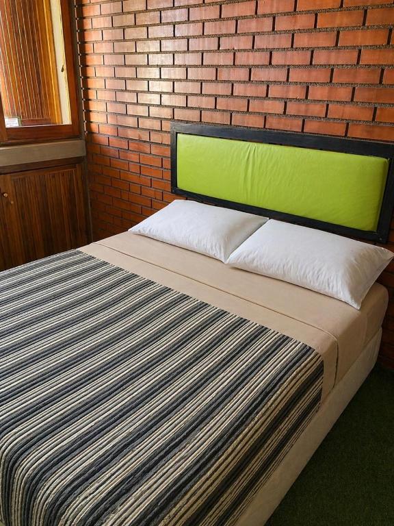 a bed with a green headboard next to a brick wall at OlasHostel in Mendoza