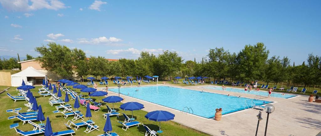 a pool with chairs and blue umbrellas and people at Borgo San Giorgio by La Principina in Grosseto