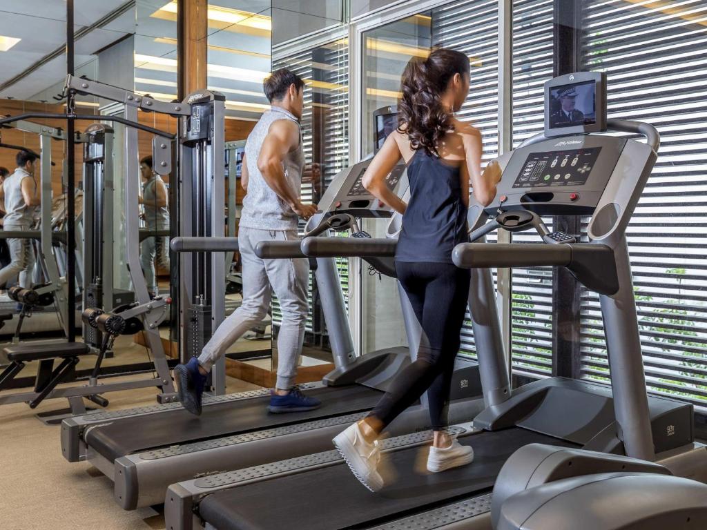 A window-lined cardio area with two occupied treadmills and additional cable equipment.