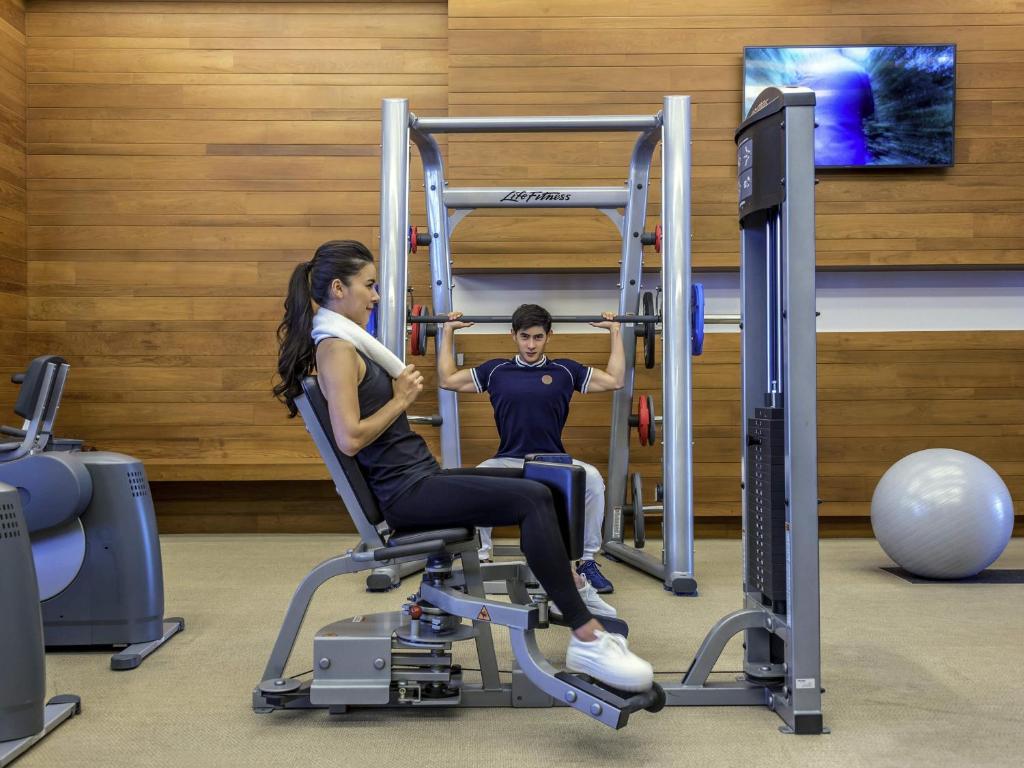 A strength-training scene centered on a multi-station machine, with a television and exercise ball nearby.