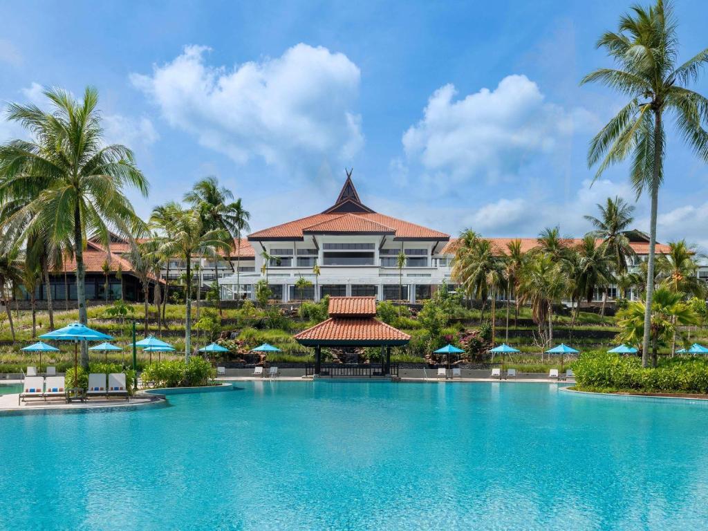 a resort with a large swimming pool and palm trees at Mövenpick Resort & Spa Bintan Lagoon in Lagoi