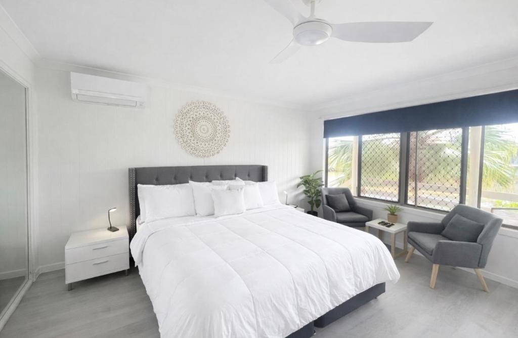 a white bedroom with a large bed and two chairs at Waters Edge in Urangan
