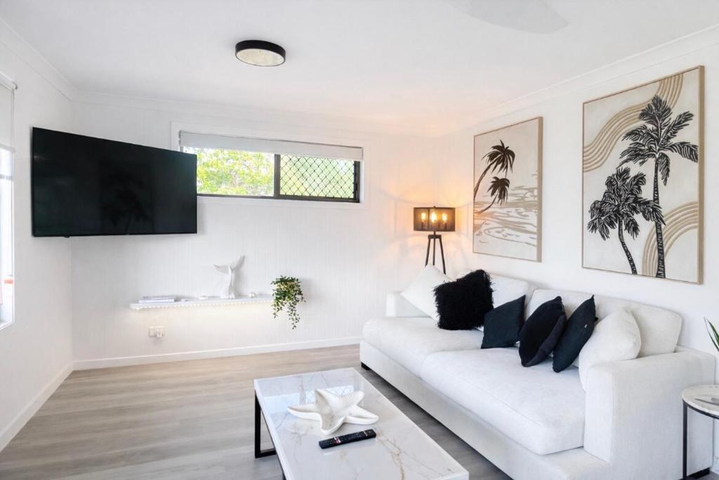 a white living room with a white couch and a tv at Lakeside Views in Urangan