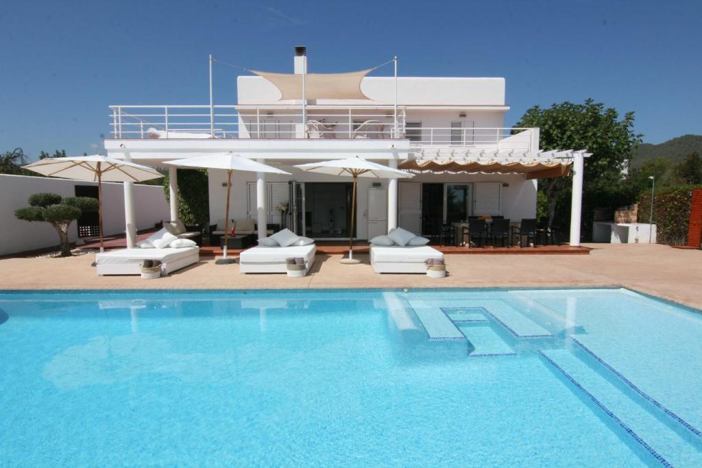 a swimming pool with chairs and umbrellas in front of a house at Villa Mara in Sant Jordi