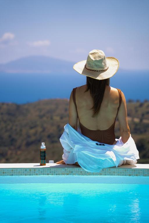 a woman in a hat sitting next to a swimming pool at Vrachos Nature Lodges PRINOS 3, Private pool in Agia Galini