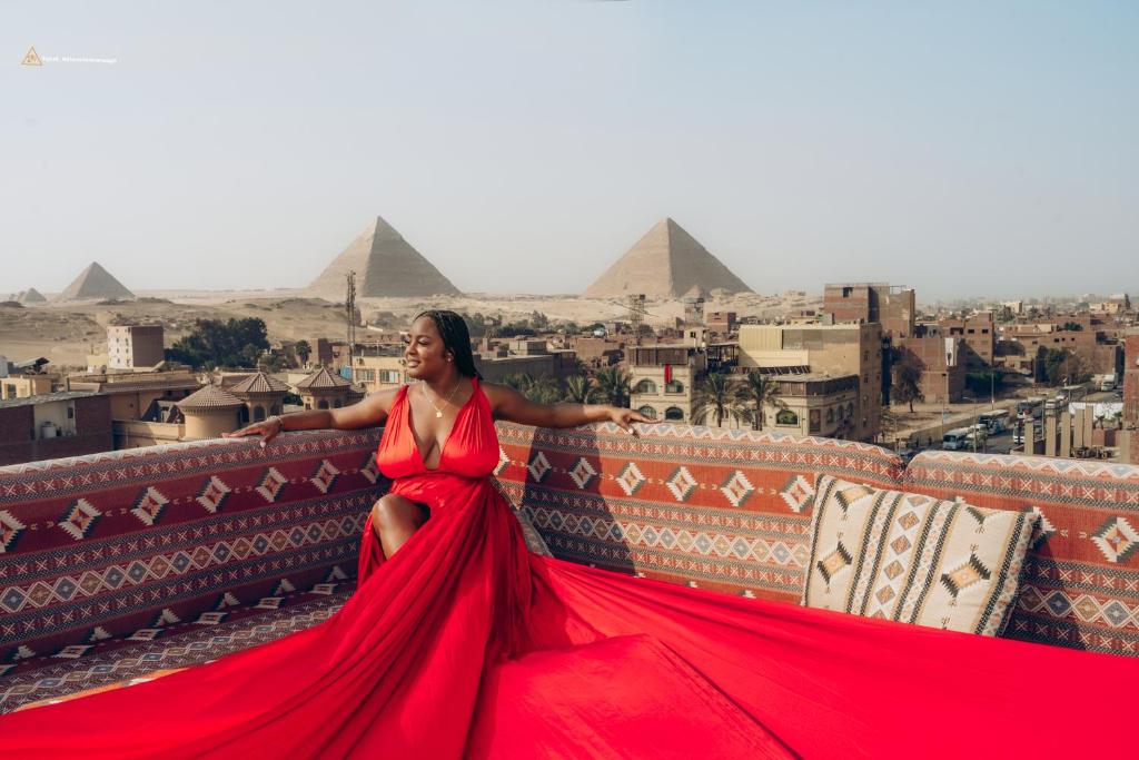 a woman in a red dress sitting on a ledge with pyramids at Solis Pyramids View Hotel in Cairo