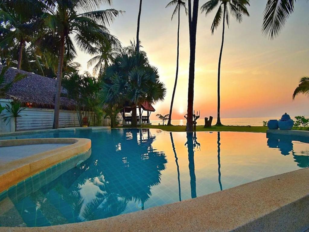 a swimming pool with palm trees and a sunset at Beachfront! 5 Bedrooms - Malee Beach Villa E1 in Ko Lanta