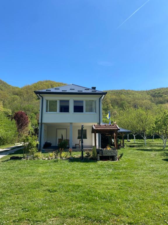 a house on a field of grass with a hill in the background at Apartman Anna & Kamp Elza in Bihać