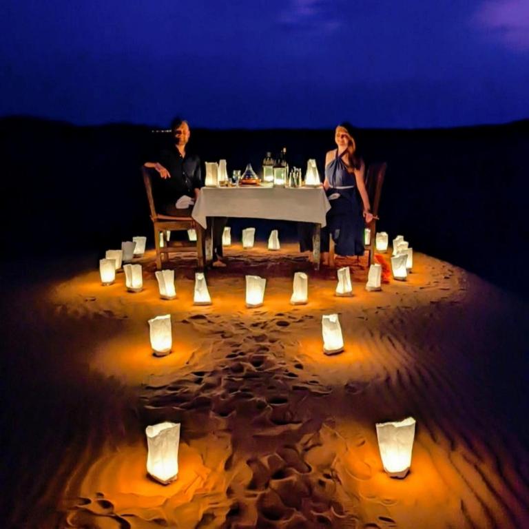 two people sitting at a table on the beach with candles at Sunrise Dunes Luxury Camp in Merzouga