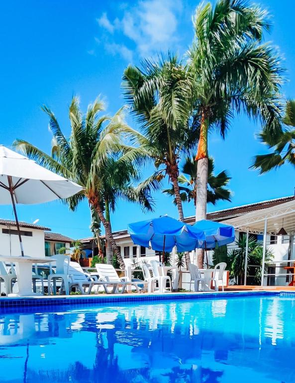 a swimming pool with palm trees and blue umbrellas at Oasis Praia Hotel in Coroa Vermelha