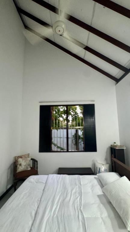 a bedroom with a white bed and a window at Induruwa Cottage in Induruwa