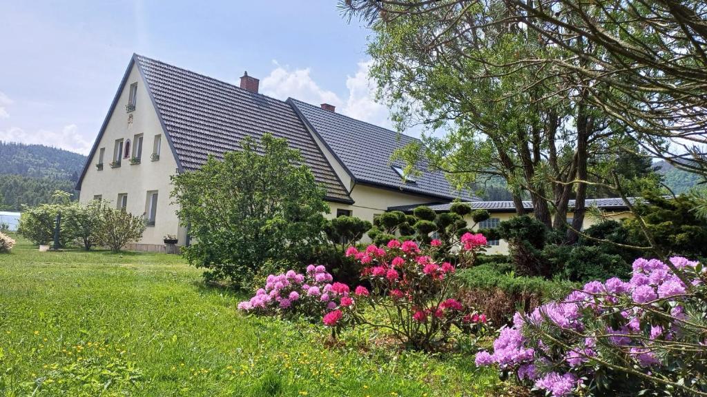 a white house with flowers in the yard at Agroturystyka Pod Leszczyną in Wambierzyce
