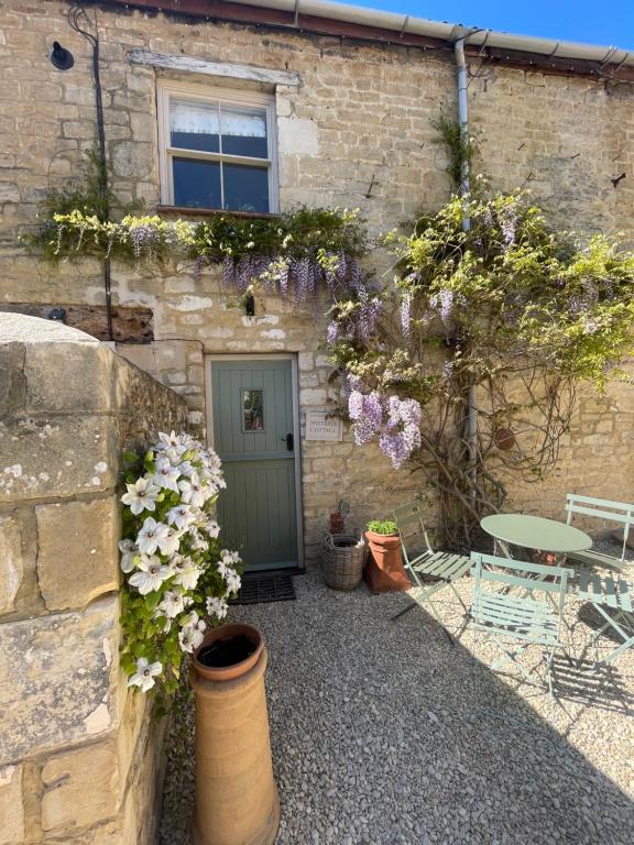 a building with a table and flowers in front of it at Wisteria Cottage - 2 bed near Bath & many NT sites in Holt