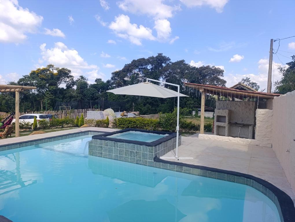 a swimming pool with an umbrella next to a building at Estância Serra Du Capiau 01 in Mairiporã