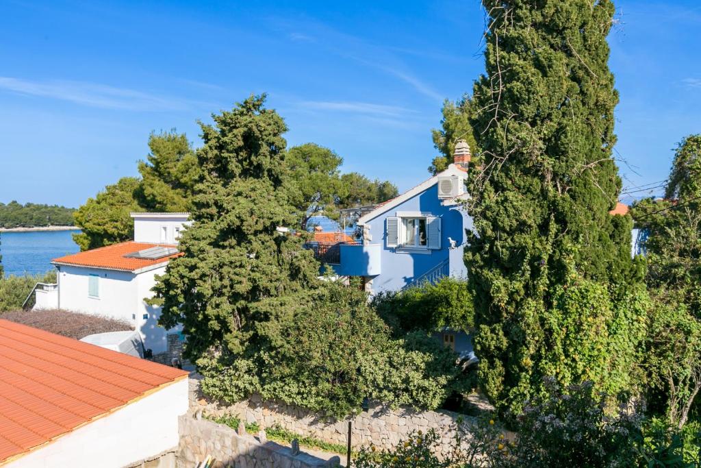 a blue house surrounded by trees and the water at Apartments by the sea Maslinica, Solta - 14748 in Maslinica