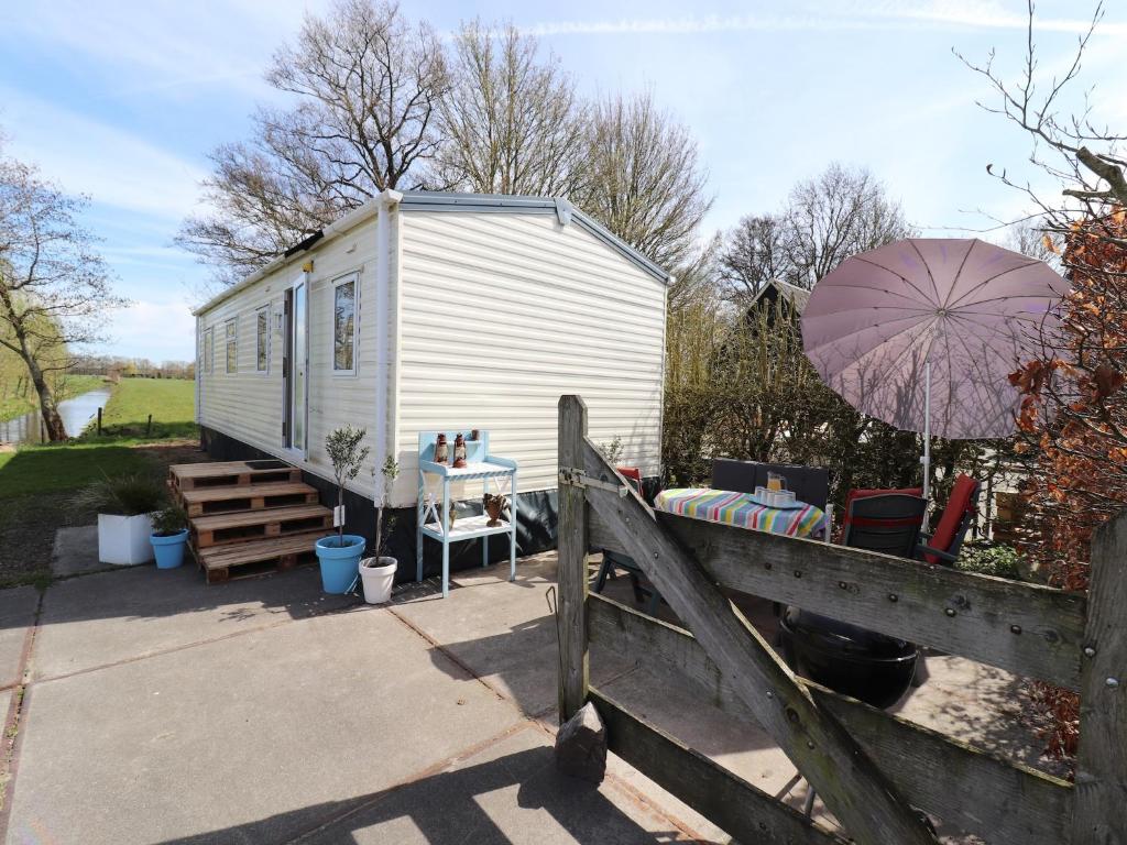a small white trailer with an umbrella and a fence at Cozy chalet with a view over the fields in Drachten