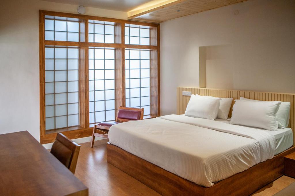 a bedroom with a bed and a table and windows at Ruscello in Pālampur
