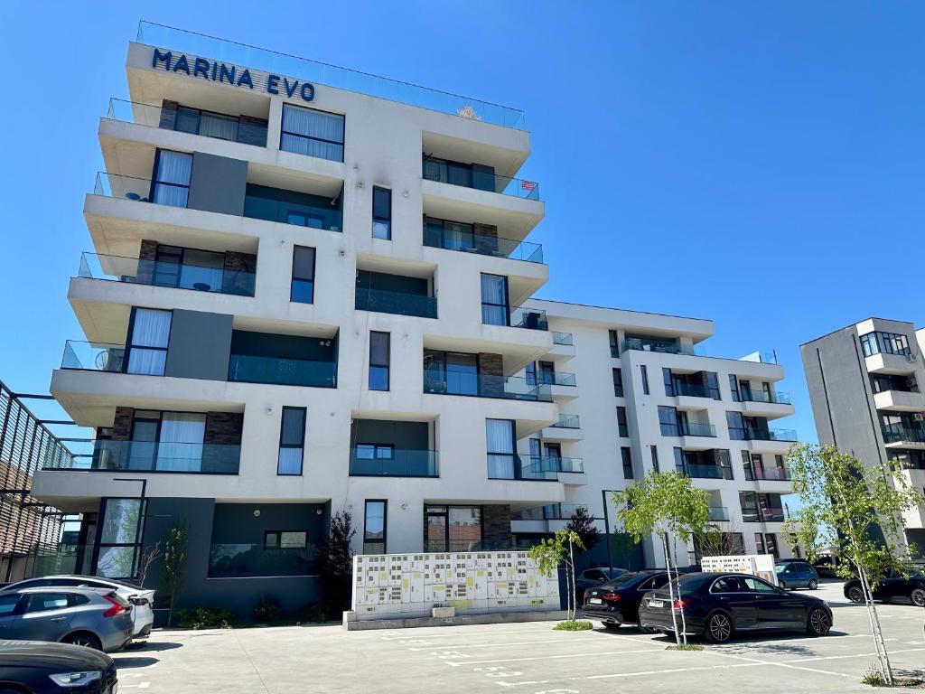 a tall white building with cars parked in a parking lot at Marina Evo Apartments in Mamaia Sat/Năvodari