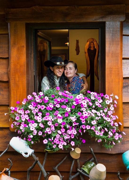 a man and woman standing behind a window with flowers at Agroturystyka na Podlasiu Kraina Puszczyka-Puszczykówka Biebrza, Augustów in Pokośno