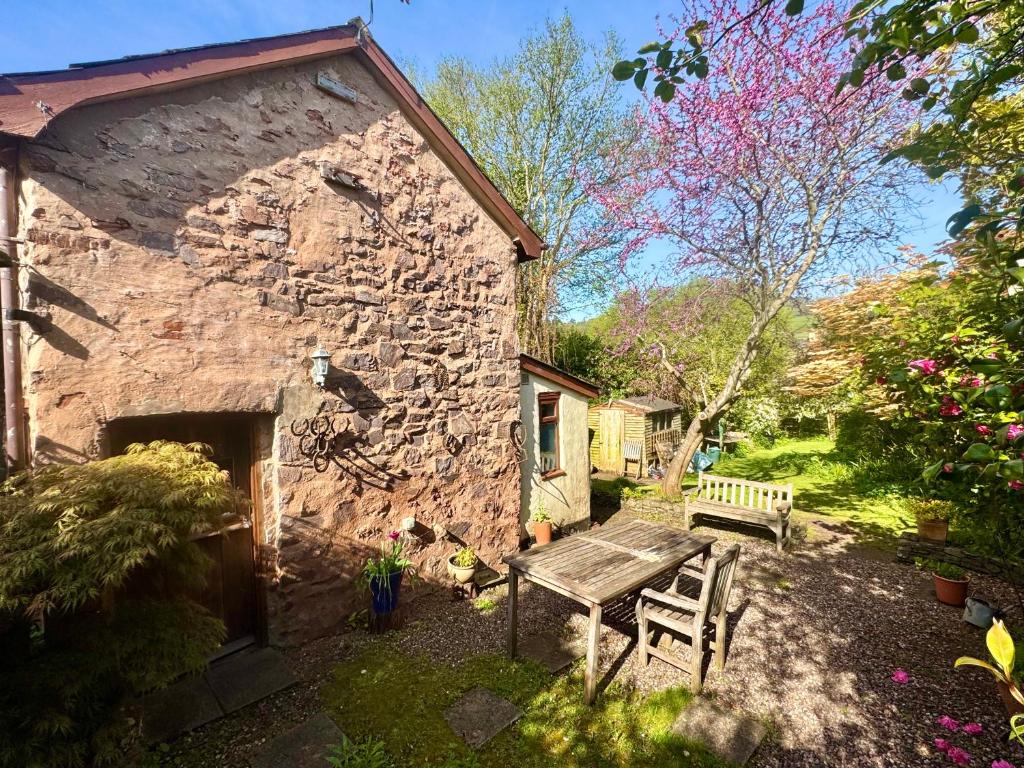 a stone building with a wooden table and a bench at Garden Cottage Wiveliscombe in Wiveliscombe