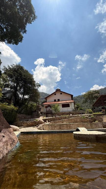 a house in the background with a pond of water at Refúgio na Serra - natureza e conforto in Teresópolis