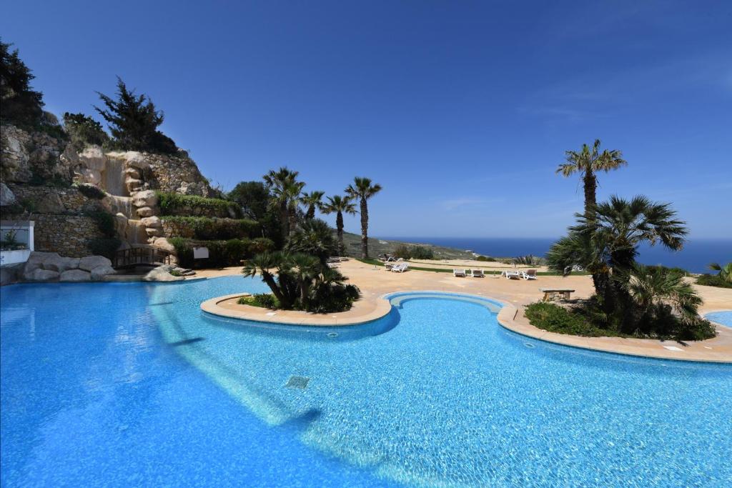 a large swimming pool next to a beach with palm trees at Hal Saghtrija - Gozo Hideaways in Żebbuġ