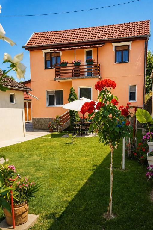 a house with a green yard with a tree and red flowers at Kuća Amazonija in Apatin