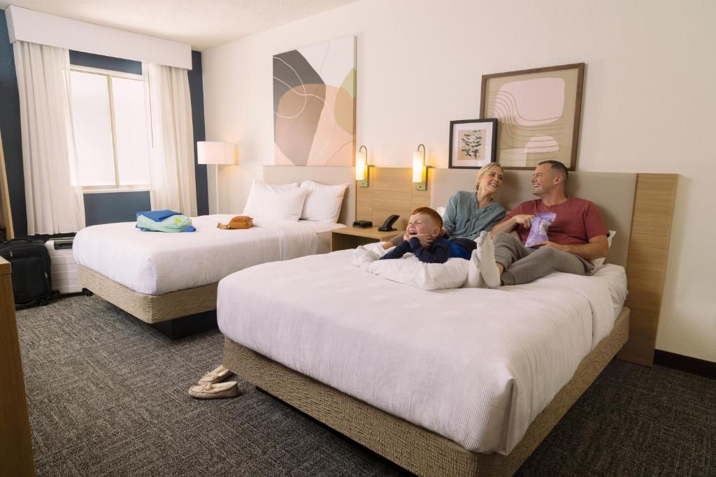 three people sitting on beds in a hotel room at Spark by Hilton Tuscaloosa University in Tuscaloosa