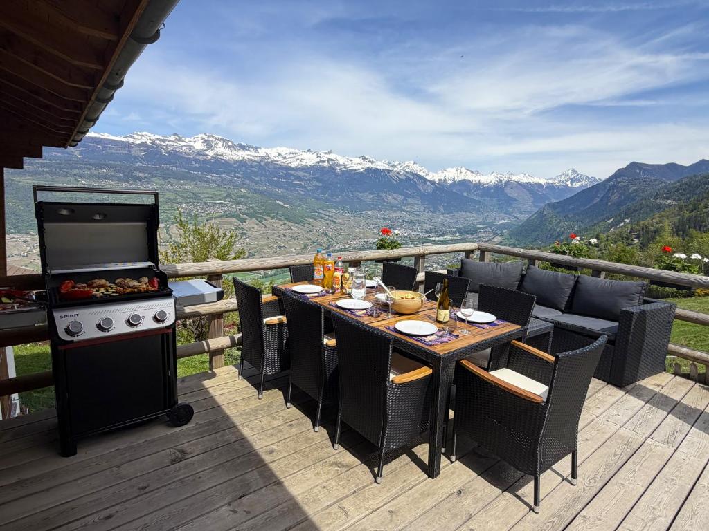 a table with chairs and a stove on a deck at Chalet panoramique avec vue alpine à 180 degrés - poêle scandinave & nature in Grône