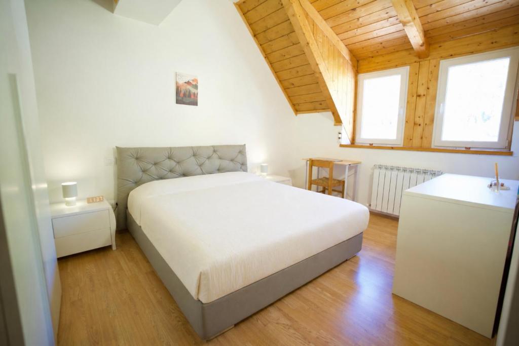 a bedroom with a white bed and two windows at Casa Azzurra - Spacious apartment in the heart of Julian Alps in Cave del Predil